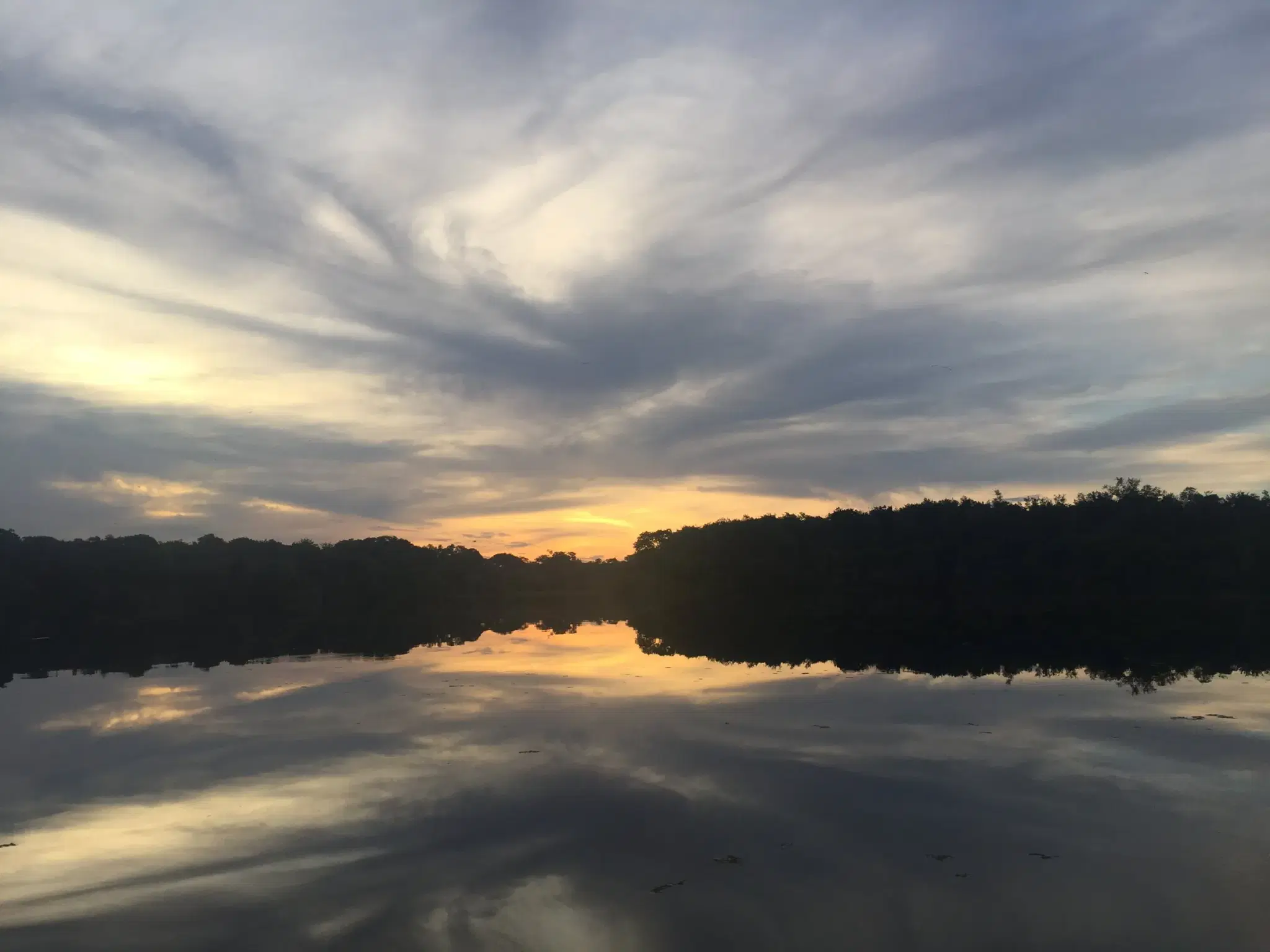 Pôr do sol sobre água parada de igarapé na região do lago Mamori, no Careiro